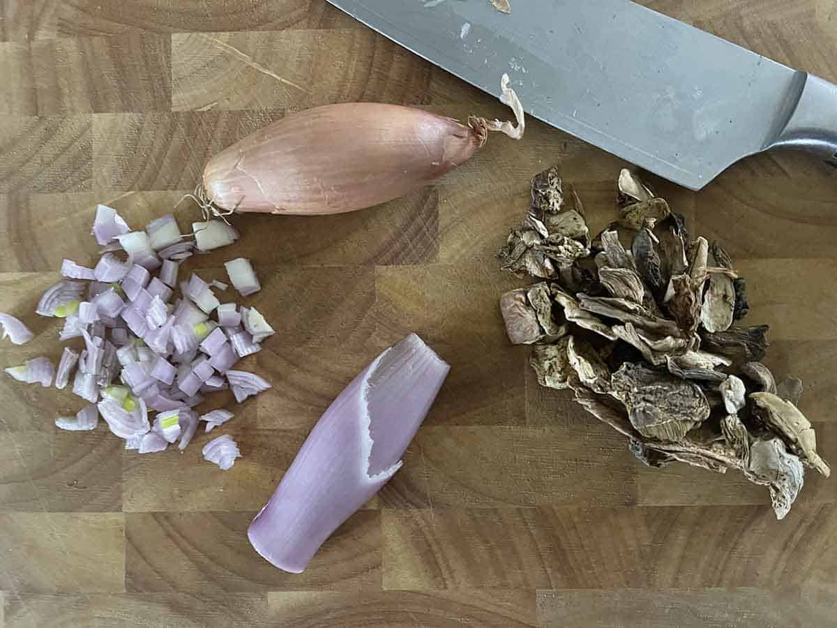 chopped shallots and dried porcini mushrooms on a board.