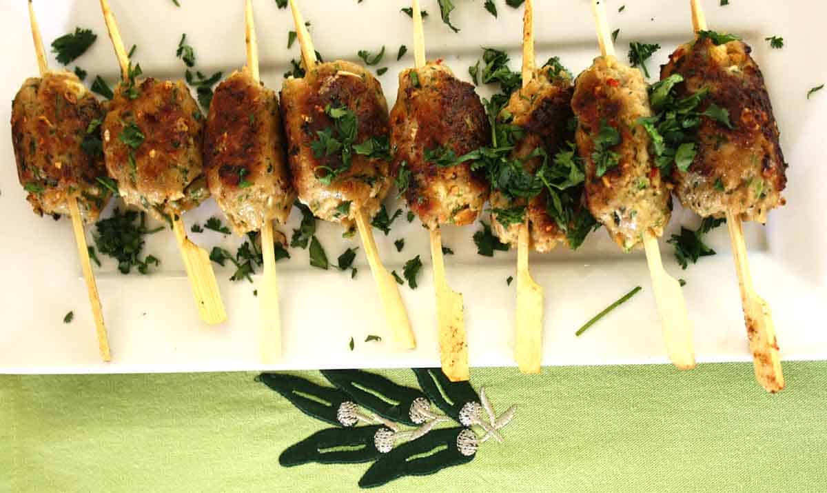 cooked pork skewers lined up on a white plate.