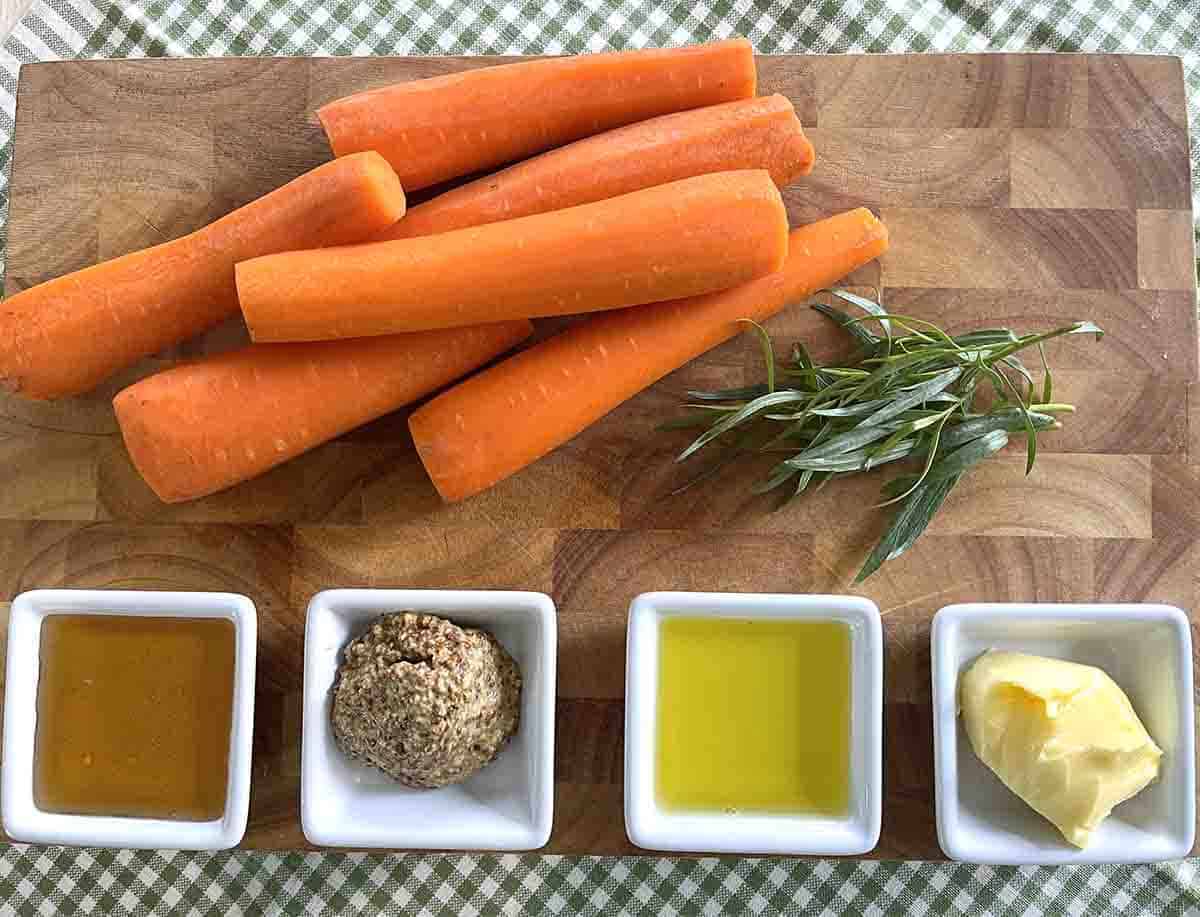 peeled carrots on a board with pots of clear honey, olive oil, butter and mustard.