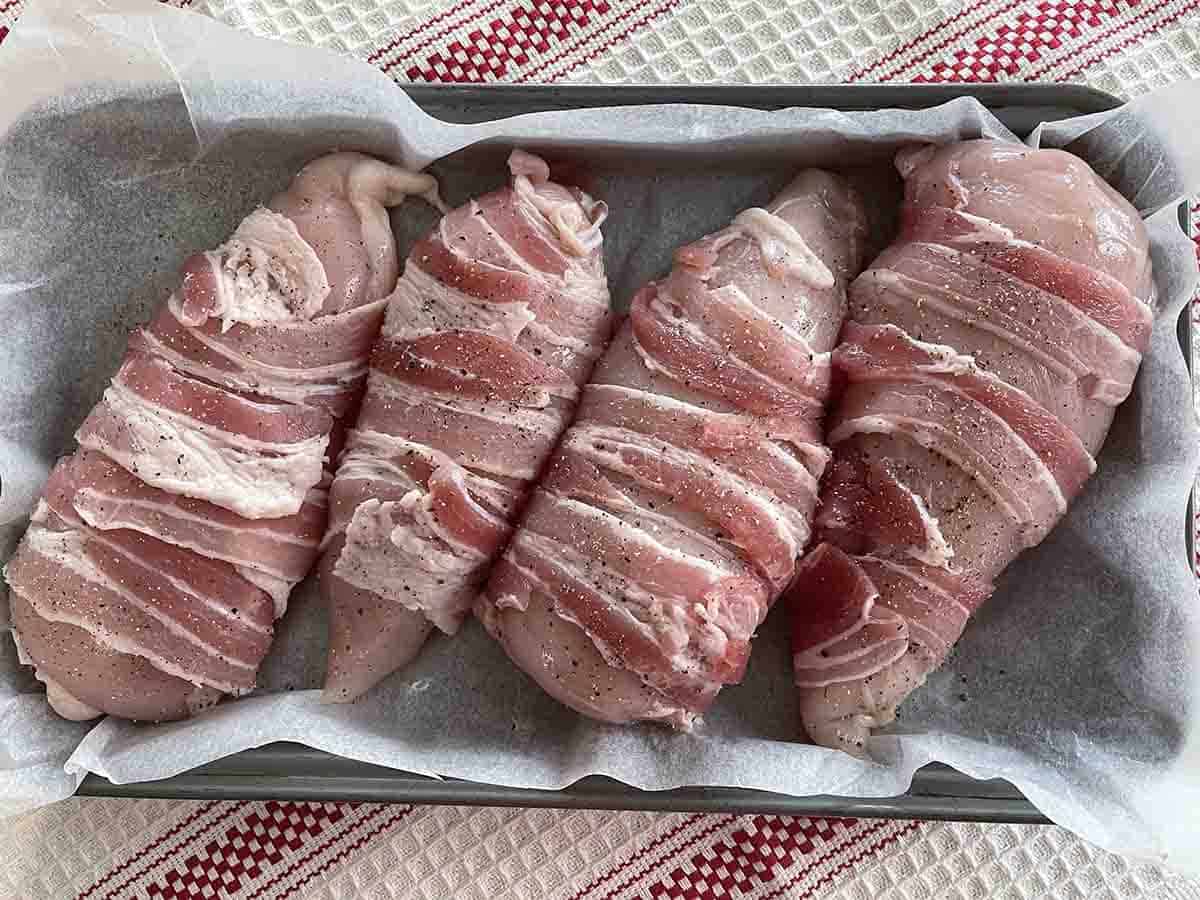stuffed chicken breasts wrapped in bacon on a tray.