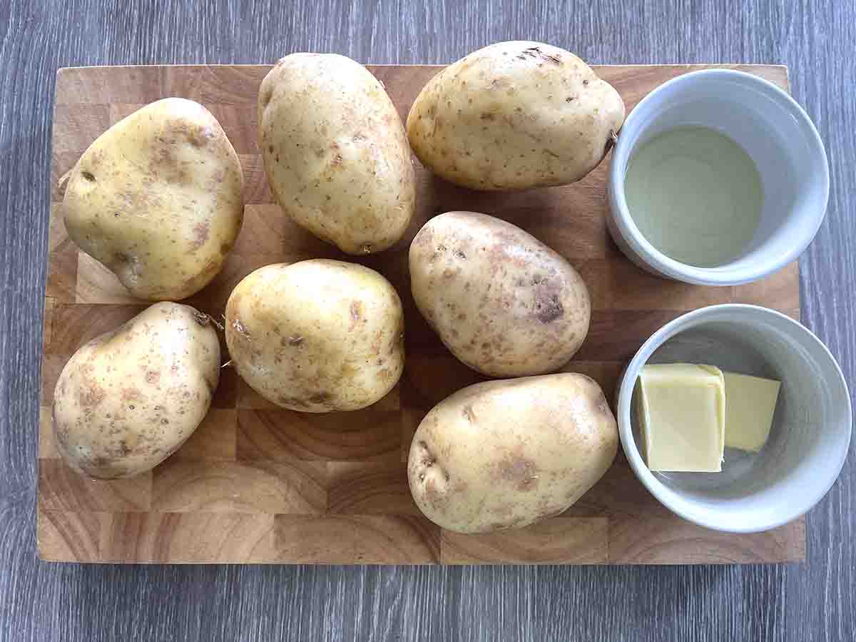 potatoes and a pot of oil and pot of butter on a board.