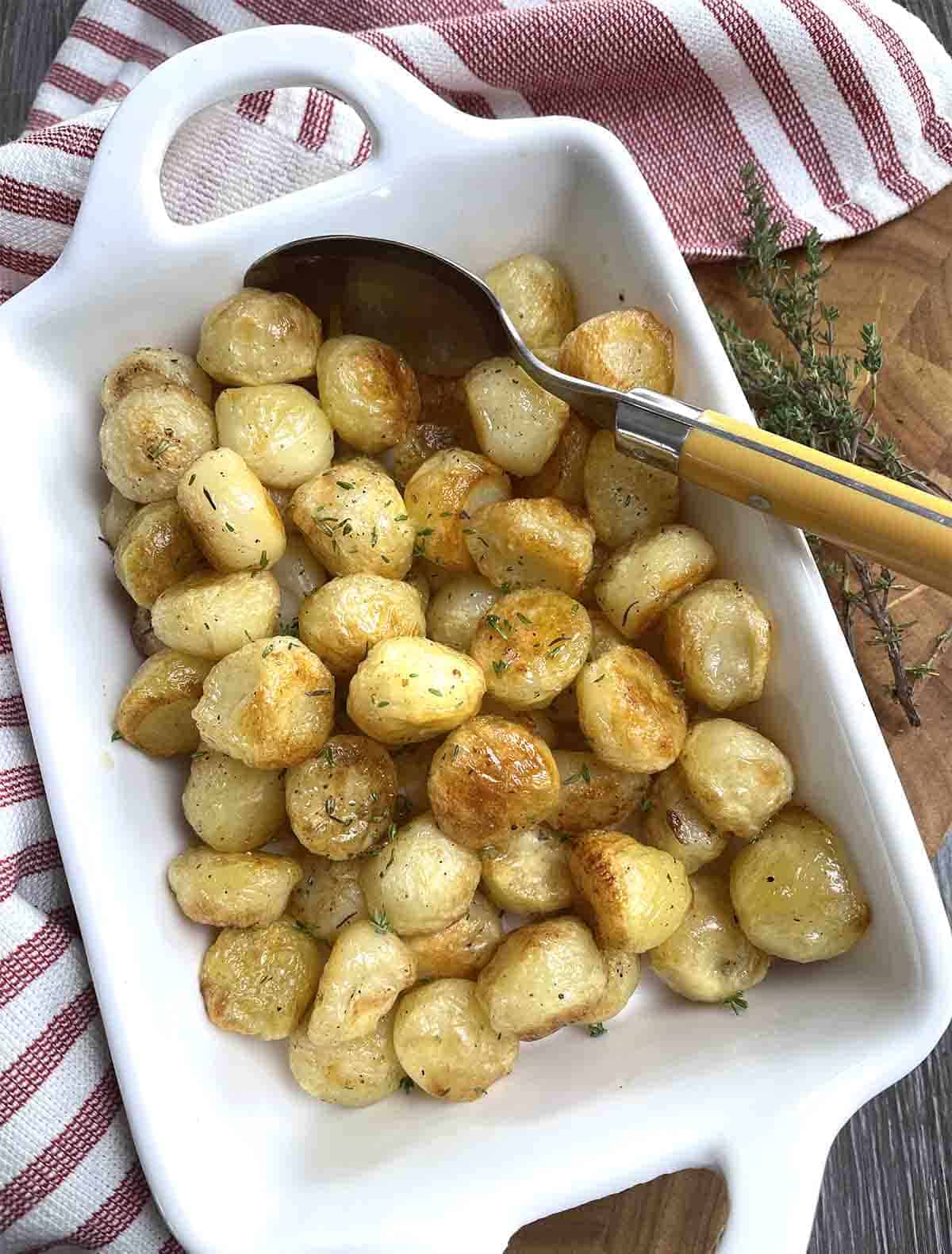 Potatoes Parisienne in a white serving dish with a spoon.