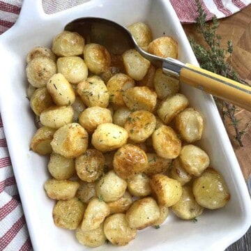 Potatoes Parisienne in a white serving dish with a spoon.