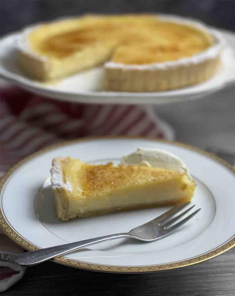 slice of lemon tart on a plate with remaining tart on a stand in the background.