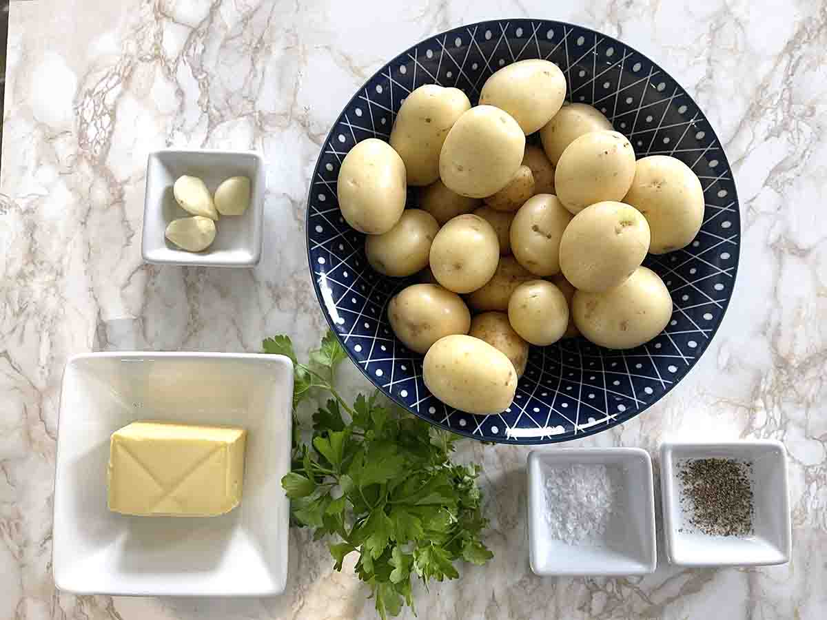 ingredients, including a bowl of potatoes, garlic, butter, oil, seasoning and parsley.