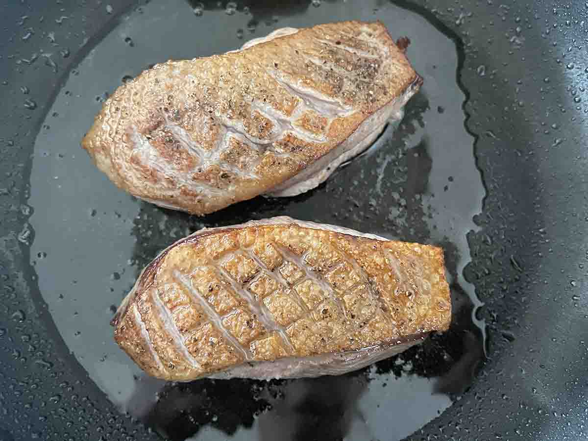 duck breasts cooking in a pan.