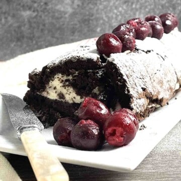 chocolate roulade on a plate with cherries on the side.