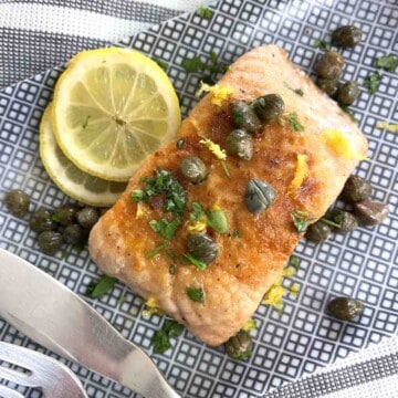 salmon meuniere on a plate with lemon slices.