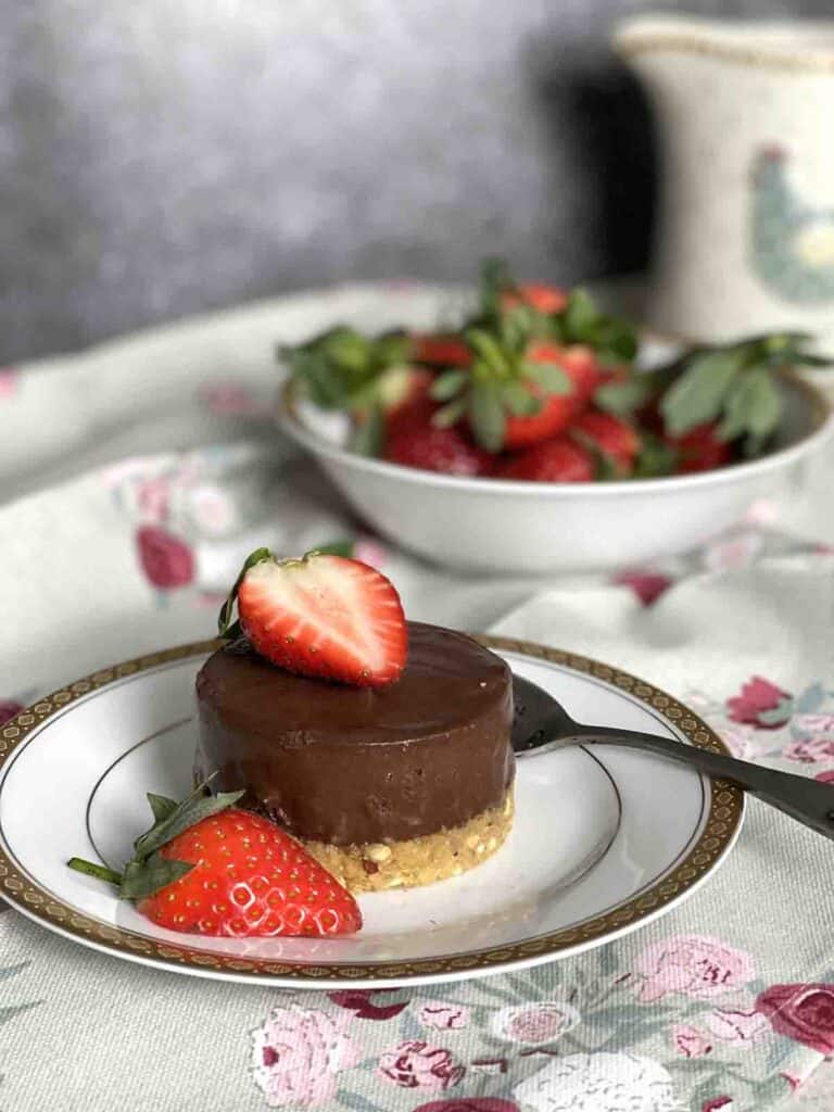 chocolate dessert on a plate with strawberries in the background.