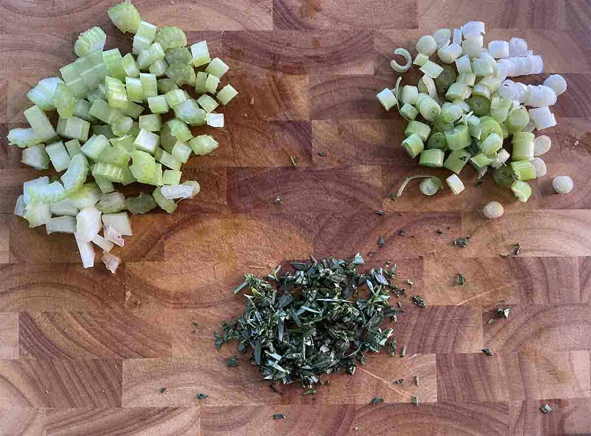 chopped celery, spring onions and tarragon on a board.