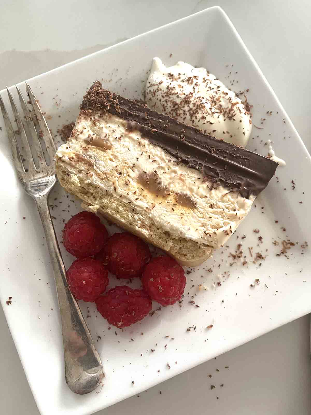 close up of slice of dessert with extra cream and raspberries.